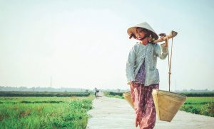 En asiatisk kvinna bär på hinkar och har hatt