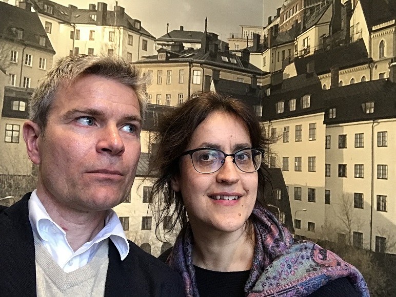 Två podcastdeltagare står framför en tapet med husfasader