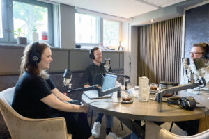 En kvinna och två män i en poddstudio