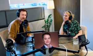 En man och en kvinna i en poddstudio med en man på skärm