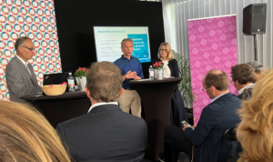 Två män och en kvinna håller föredrag från en scen med publik